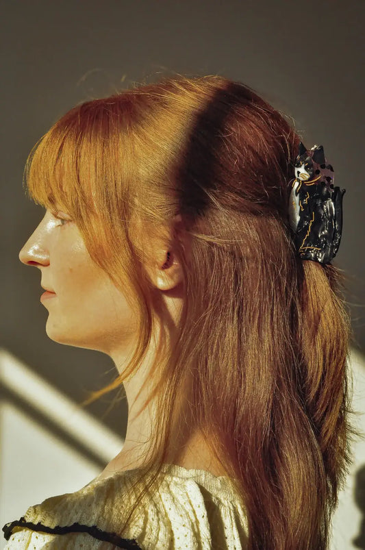 Woman with red hair tied back with a decorative hair clip, wearing a gold top.