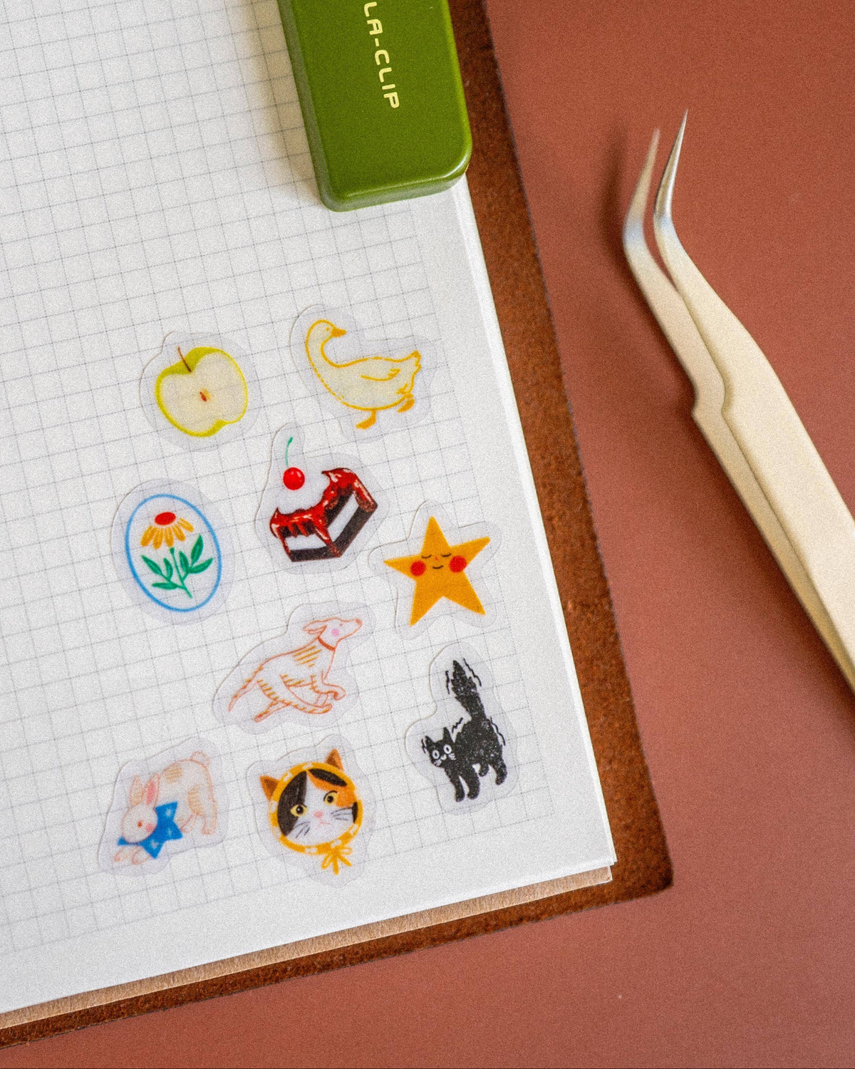 Clear stamps with various designs on a paper with a green stamping tool and tweezers.