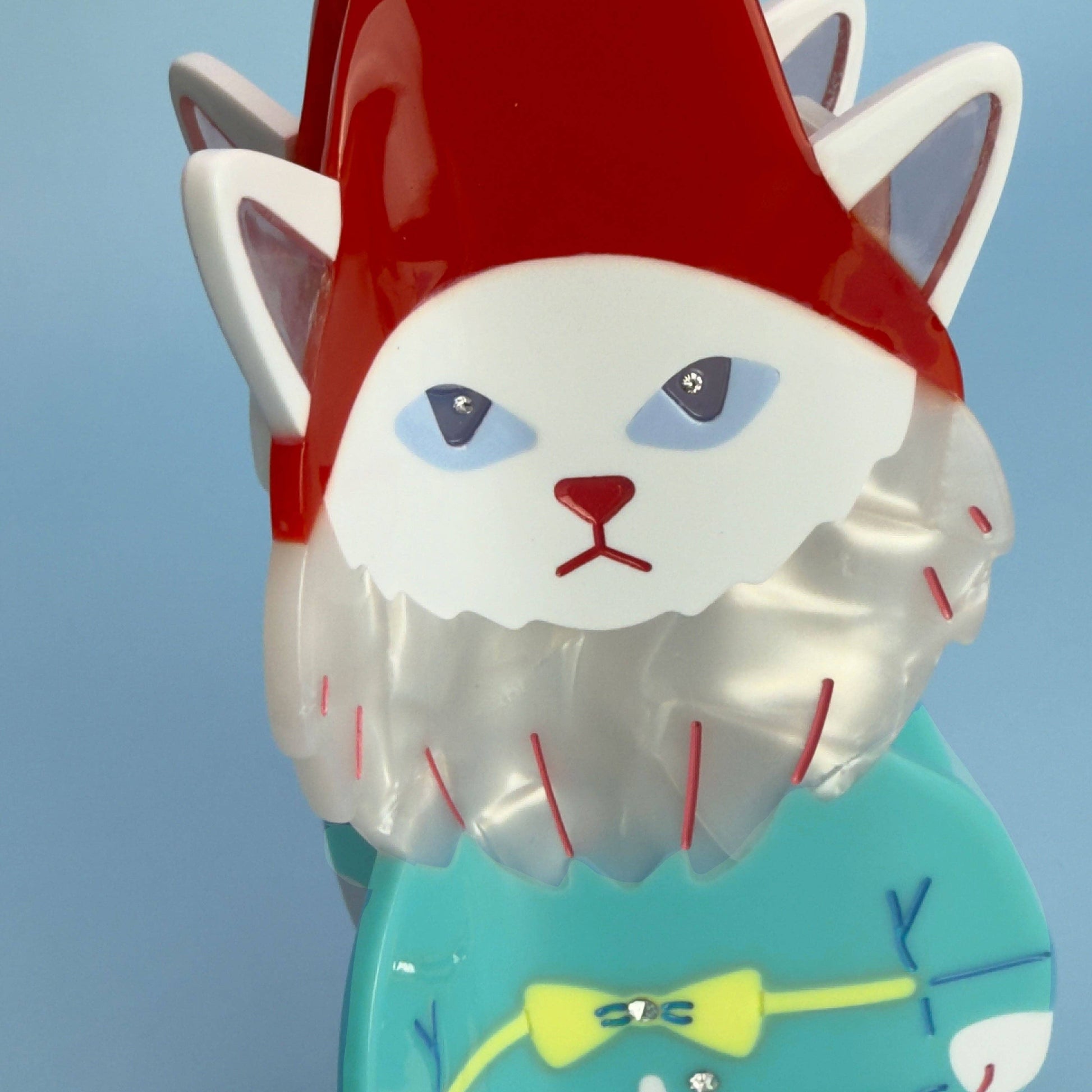 Colorful cat-shaped object with a red hat and blue eyes against a clear sky.