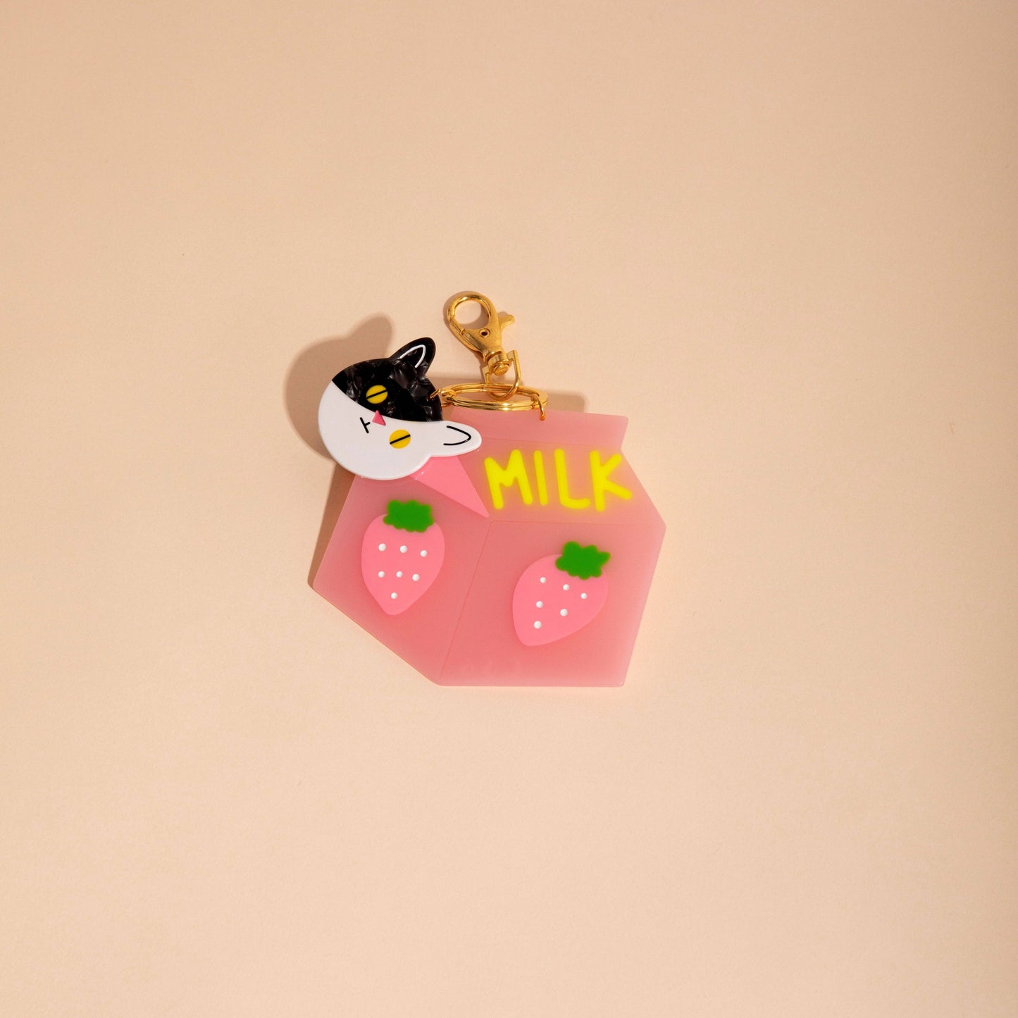 Keychain shaped like a pink milk carton with a cat face on a beige background