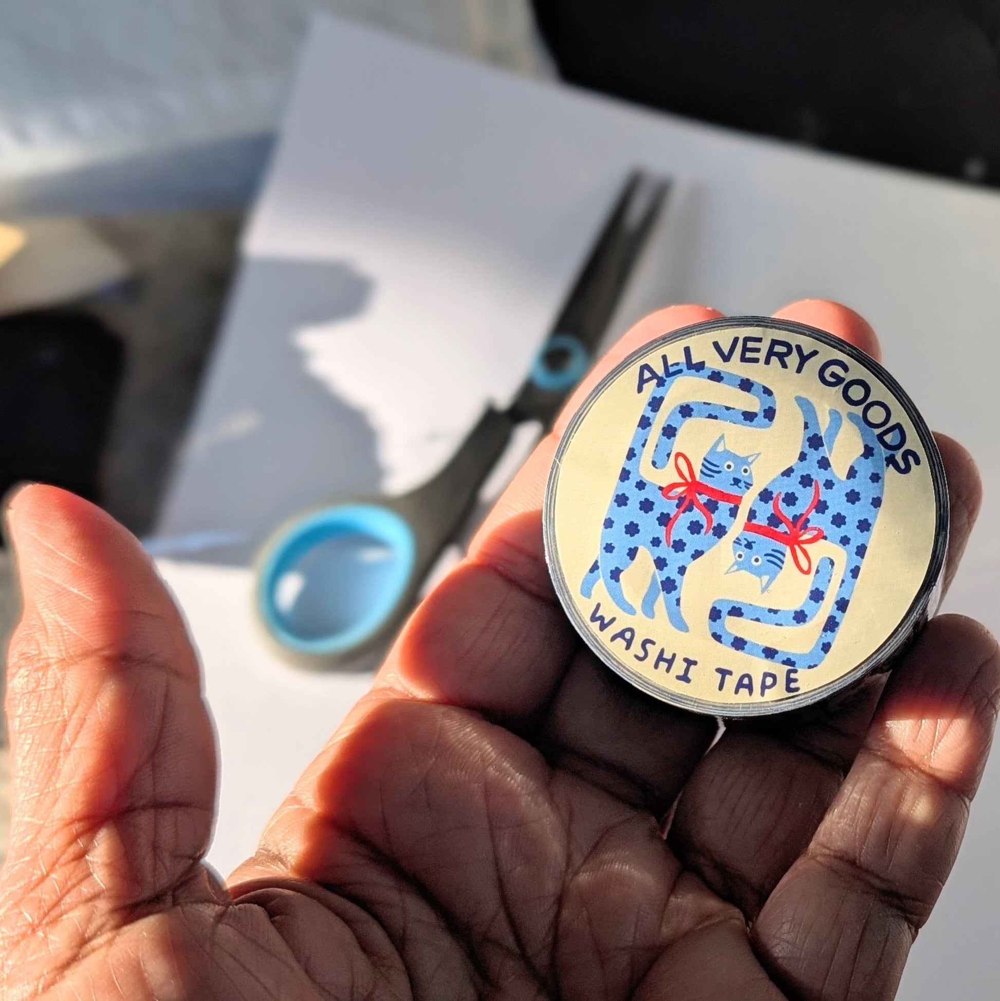 Hand holding a washi tape container with cat design, scissors in the background