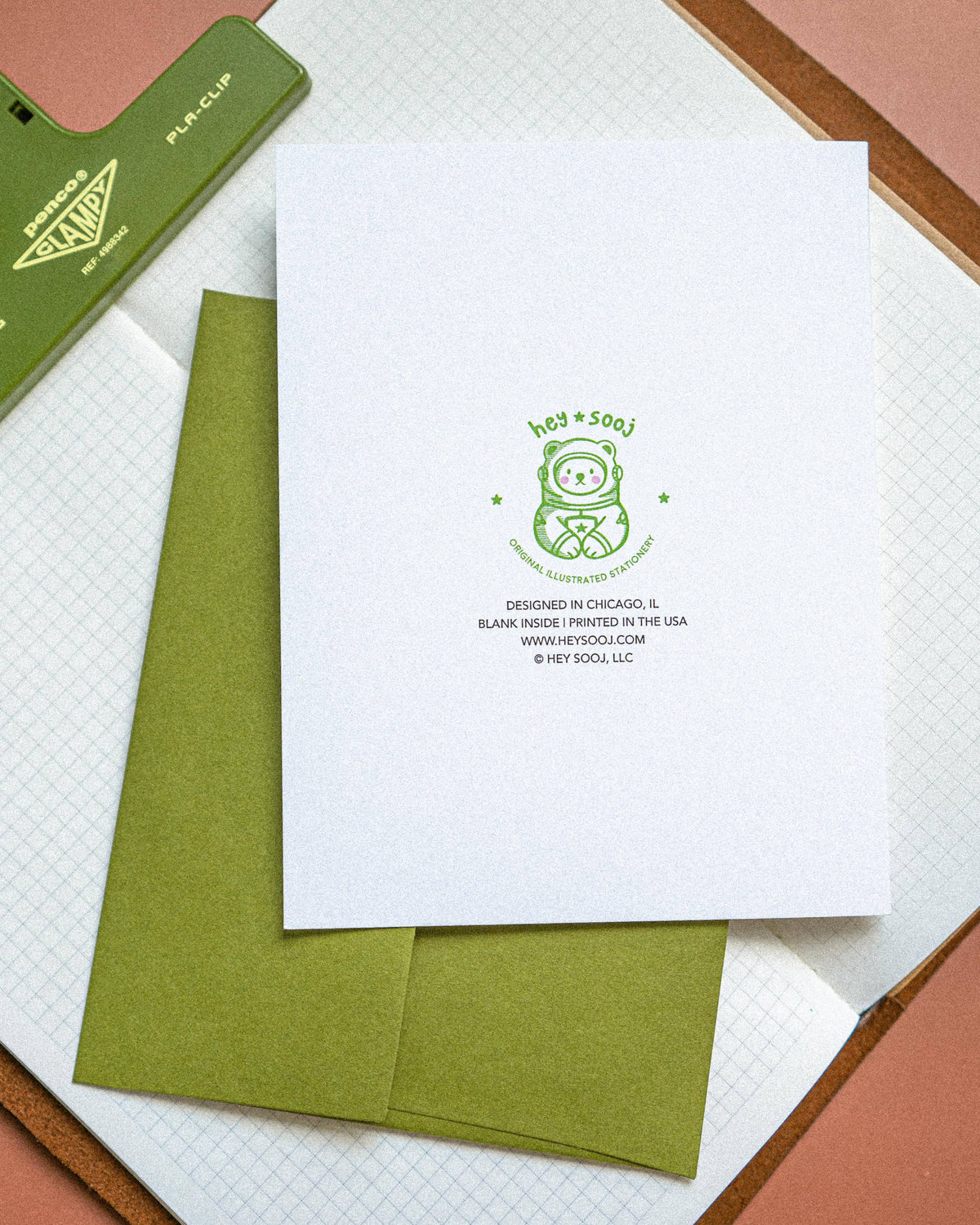 White card with green logo and text on a matching green envelope, placed on a textured surface.