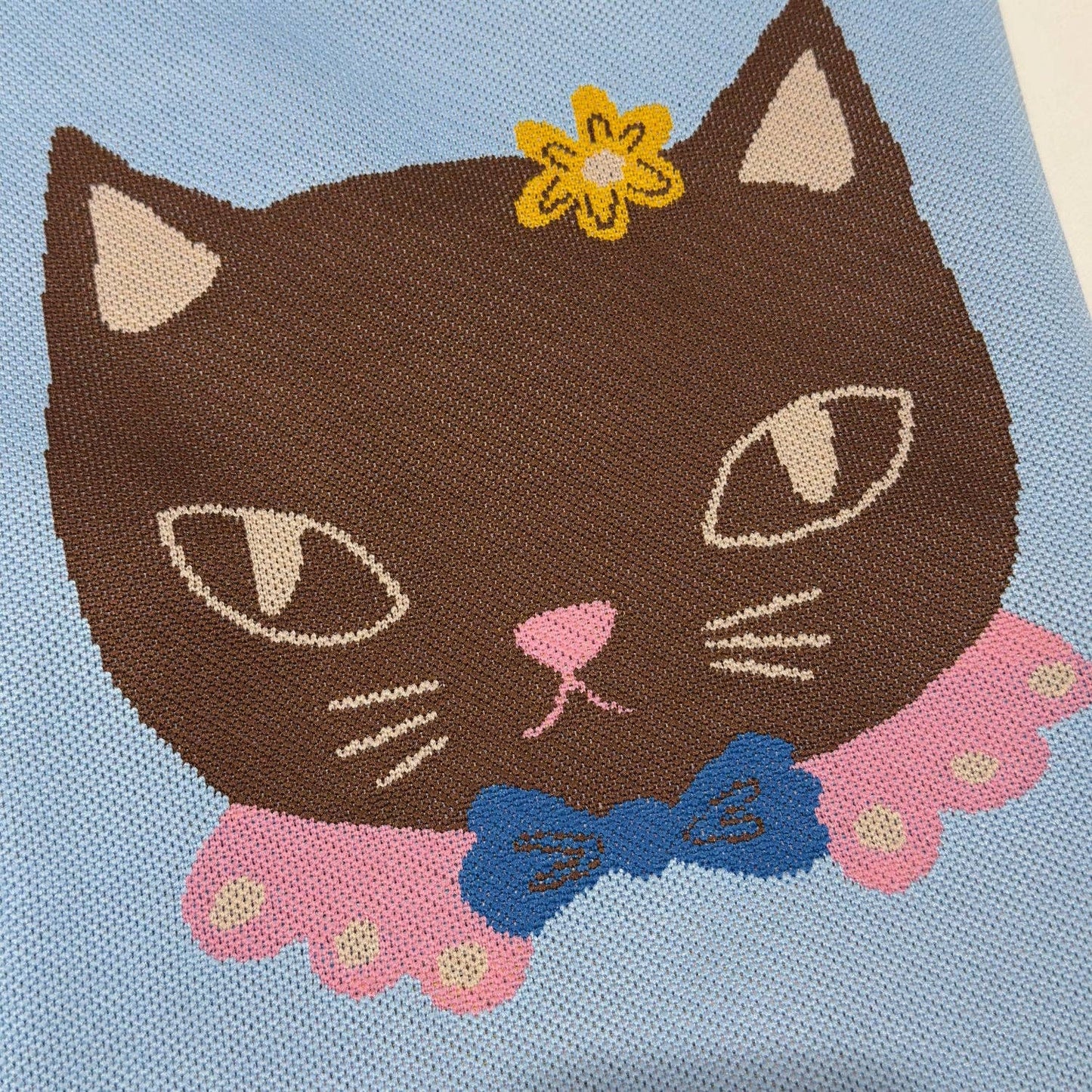 Embroidered design of a cat with a flower and bow on a blue fabric background
