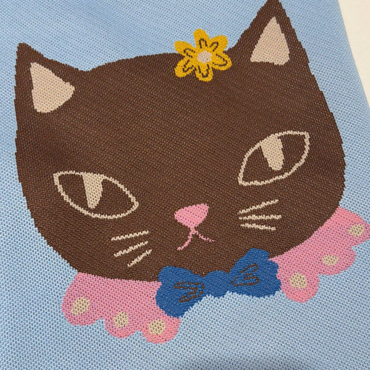 Embroidered design of a cat with a flower and bow on a blue fabric background