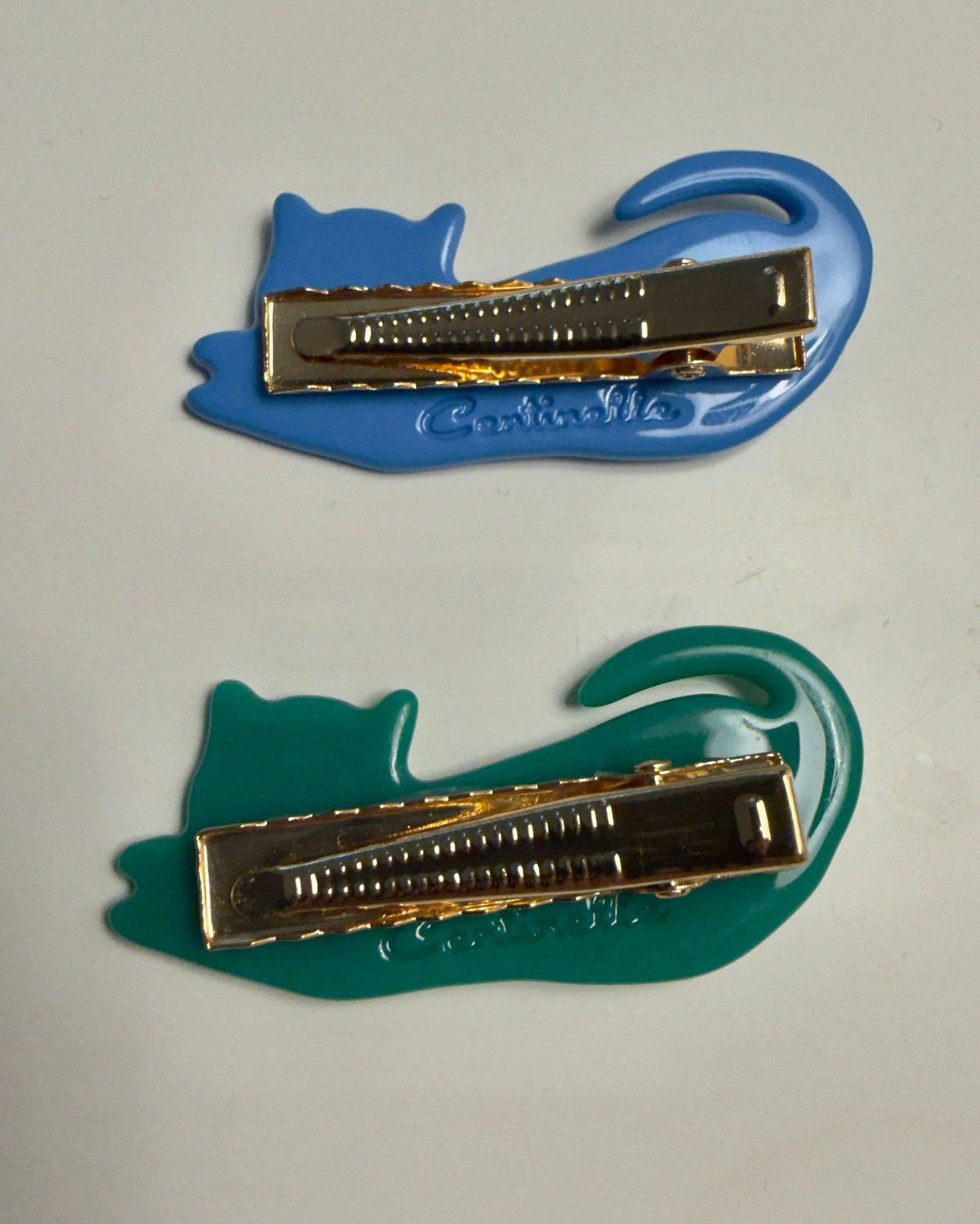 Two cat-shaped hair claw clips on a plain light background, one in blue and one in teal, both with gold-tone metal clasps. The blue clip has 'Chic Chic' embossed on the side.