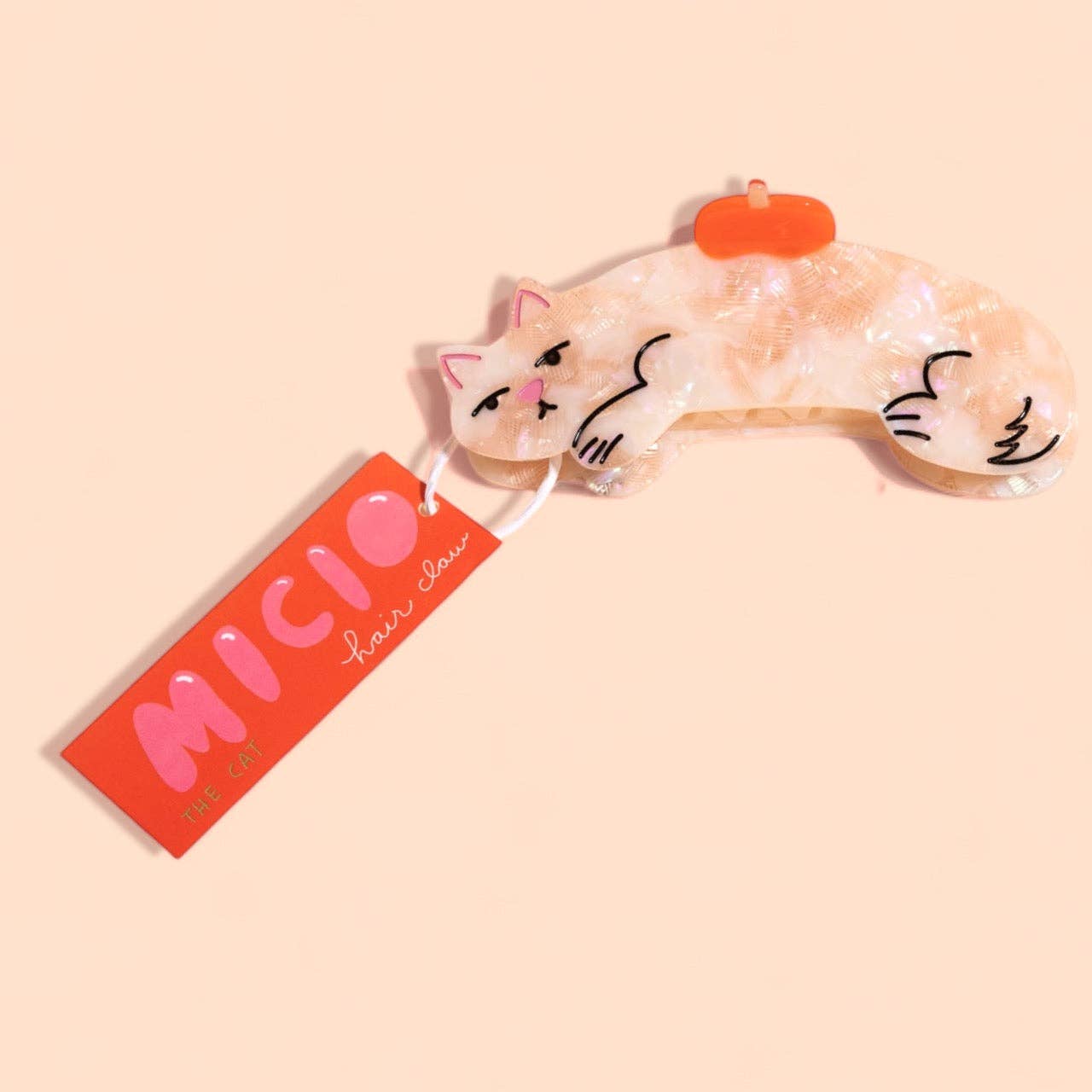 Cat-shaped hair clip with a pink label on a beige background