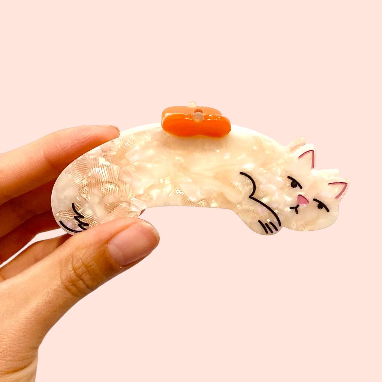 Cat-shaped hair tie held by a hand against a light pink background