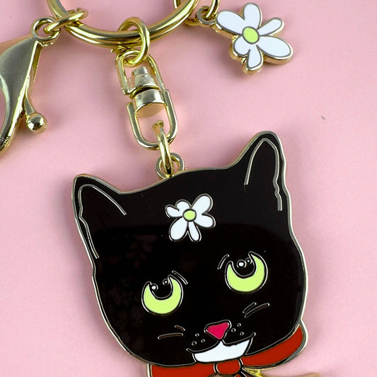 Black cat keychain with flower charm on a pink background