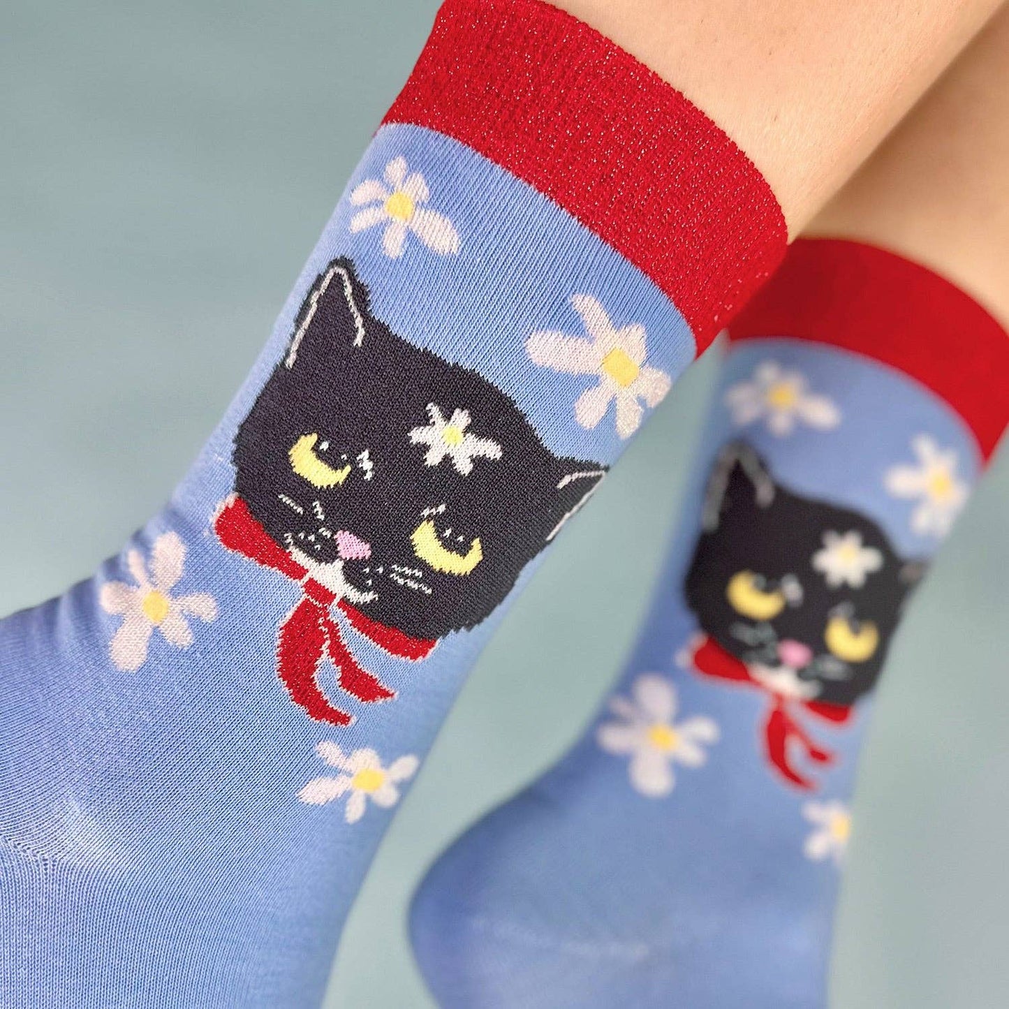 Blue socks with black cat design and red accents worn by a person.