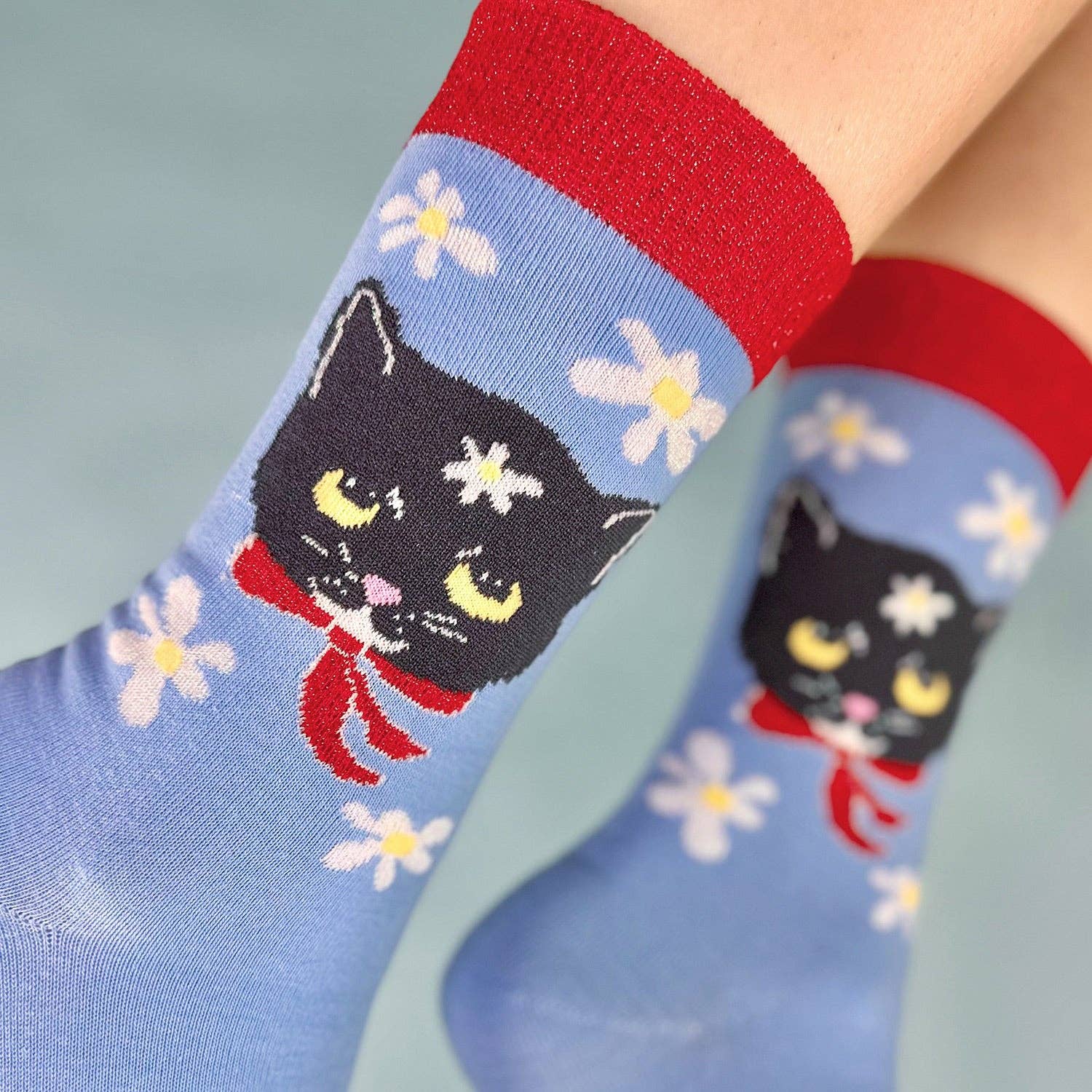 Blue socks with black cat design and red accents worn by a person.