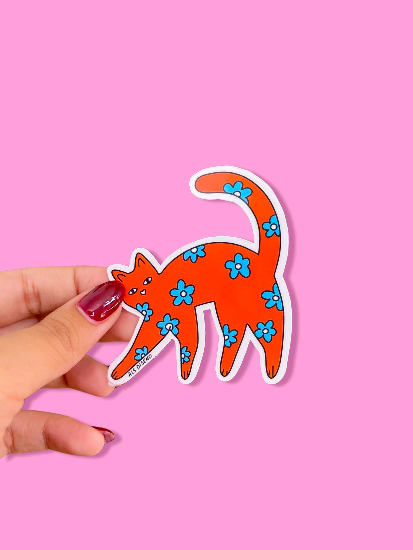 Hand holding a red cat sticker with blue flowers on a pink background
