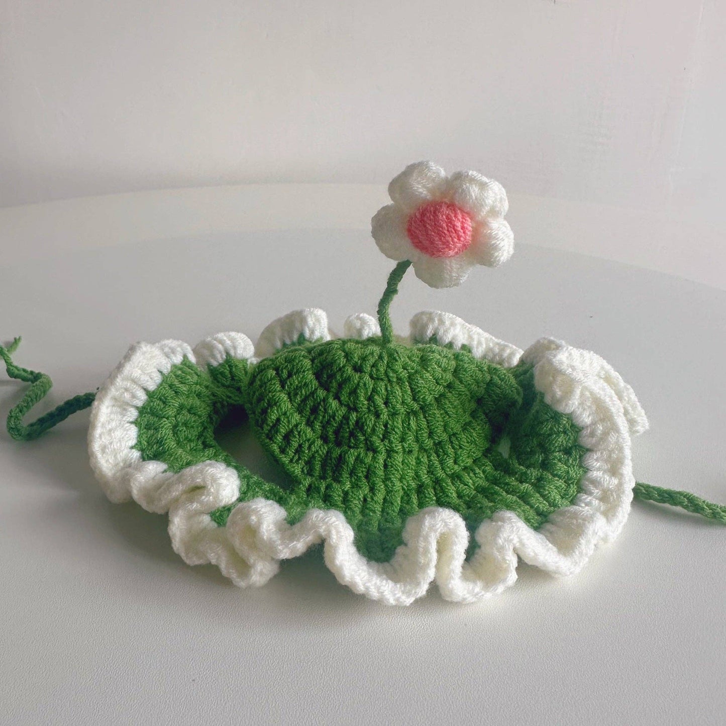 Crocheted green leaf with a white flower on a light gray background
