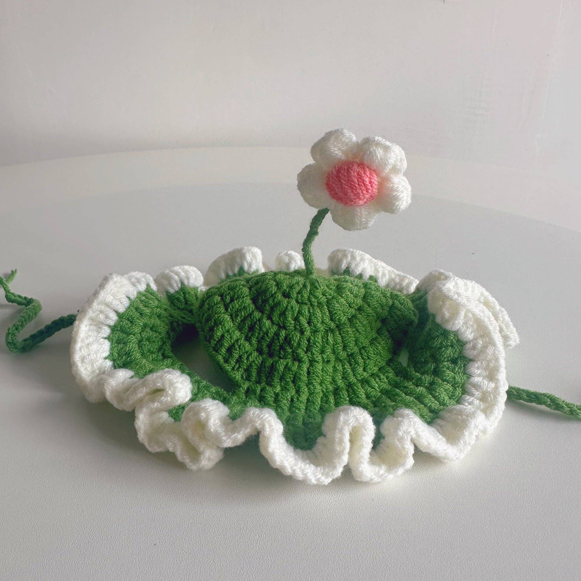 Crocheted green leaf with a white flower on a light gray background