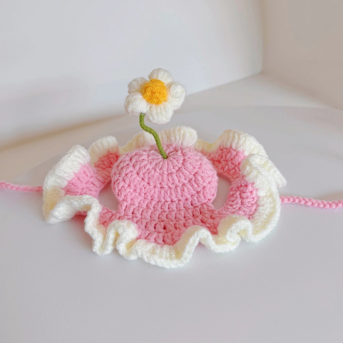 Crocheted pink and white flower with a small yellow flower on a light background