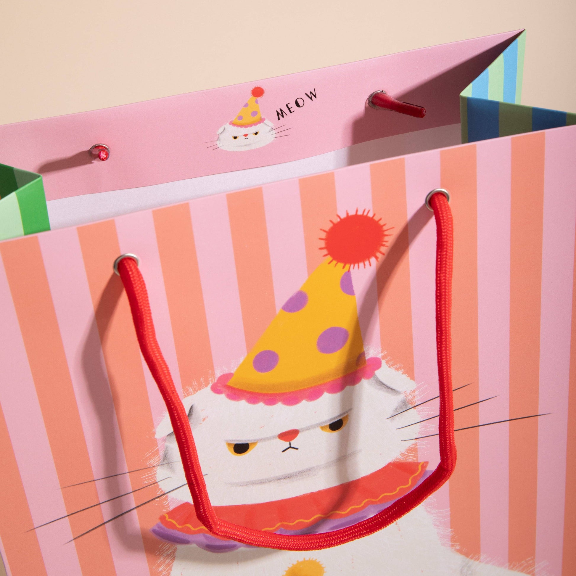 Colorful gift bag with a cat design wearing a party hat on a pink background