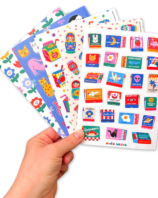 Colorful sticker sheets held by a hand on a white background