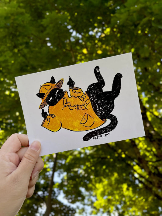 Hand holding a card with a black cat illustration against a green leafy background