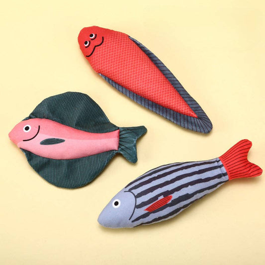 Three fish-shaped toys in red, pink, and gray on a beige background