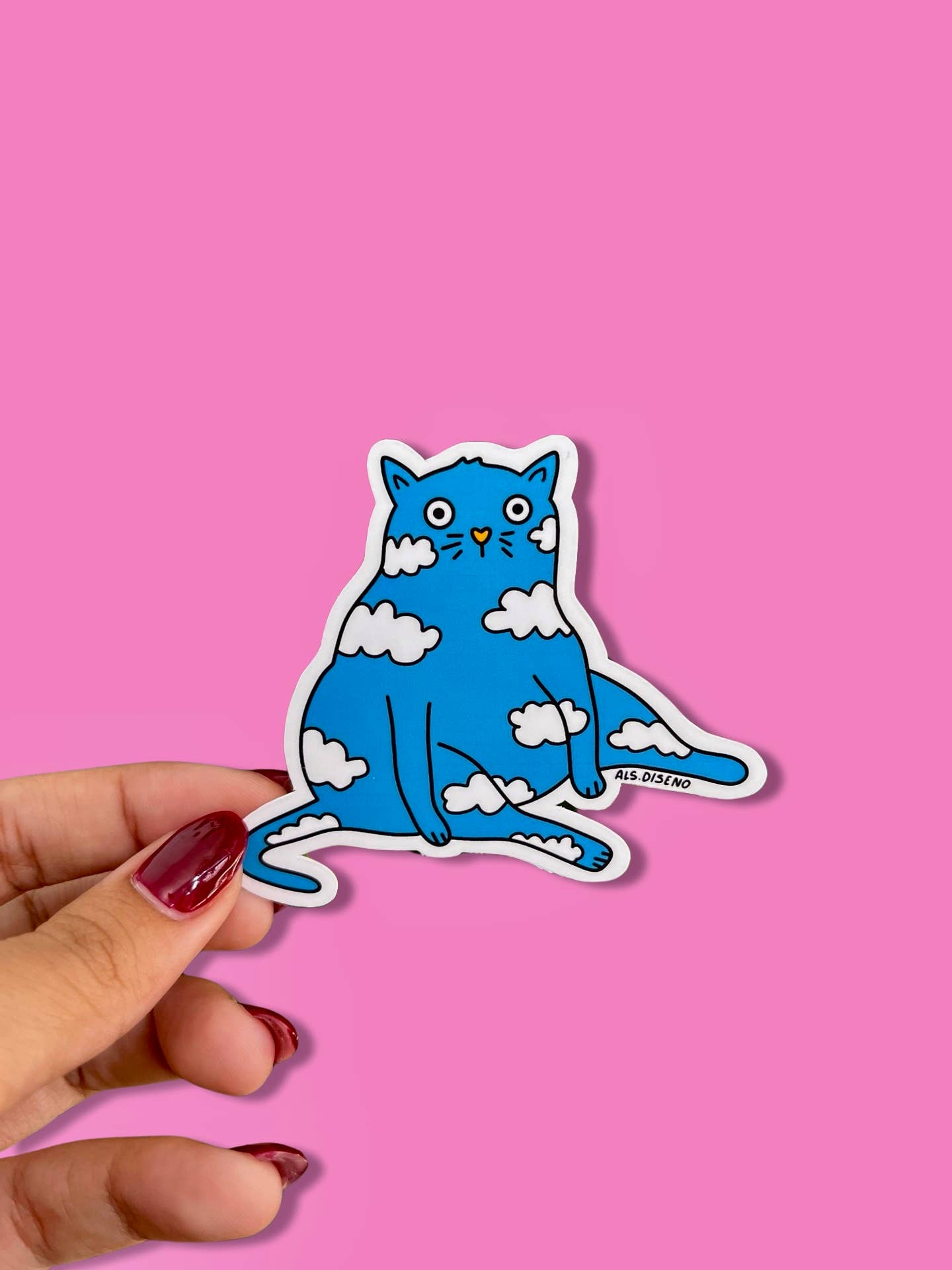 Blue cat sticker with white clouds held by a hand against a pink background
