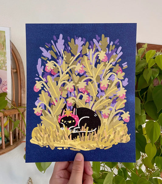 Hand holding a colorful painting of a black cat among flowers on a blue background.