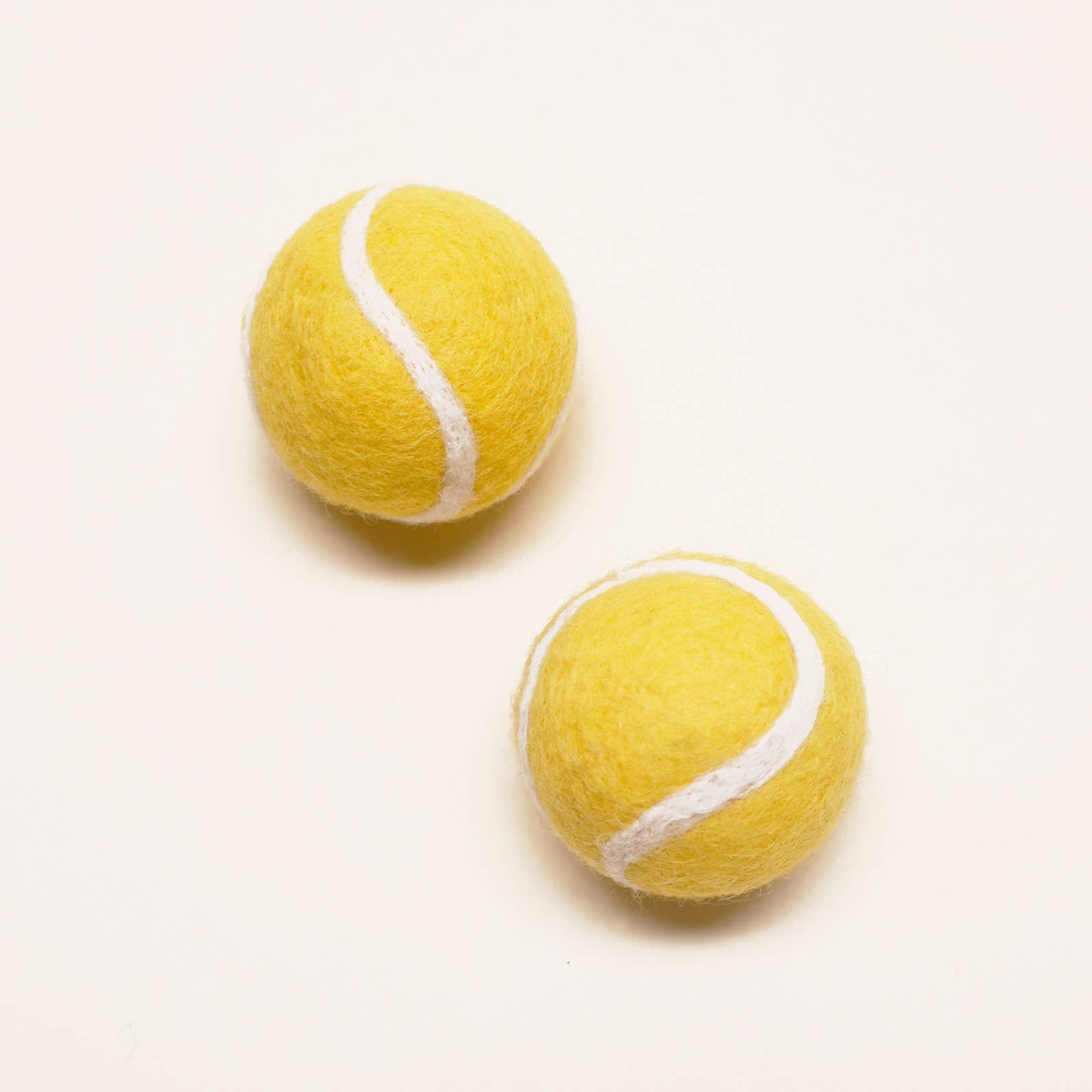 Two yellow tennis balls with white strings on a light beige background